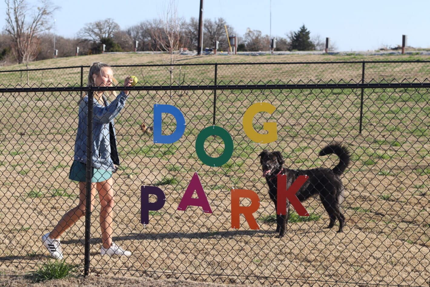 A girl and her dog are standing in front of the fence. A girl and her dog are standing in front of the fence.