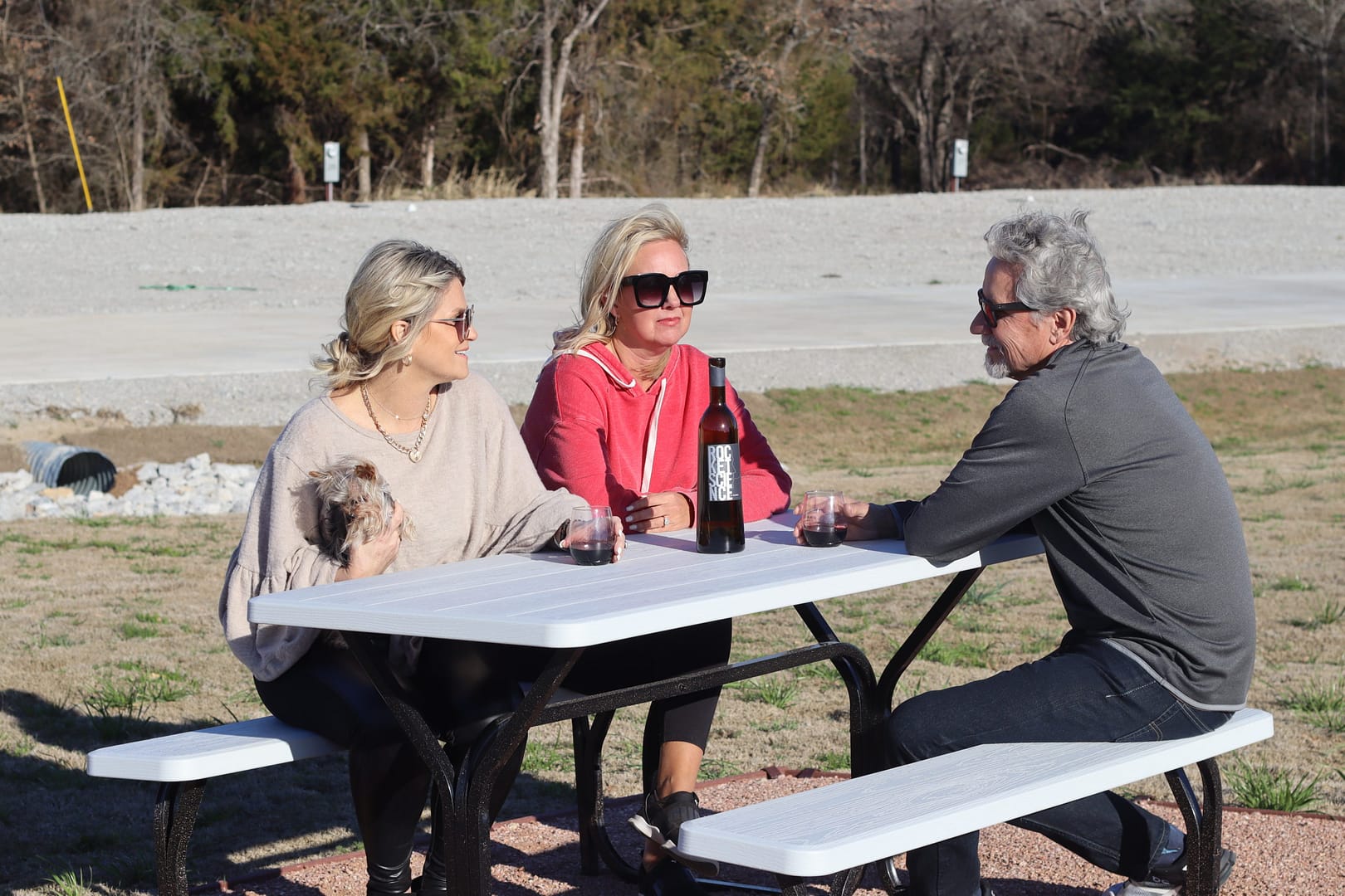 A group of people sitting at picnic tables with a dog. A group of people sitting at picnic tables with a dog.