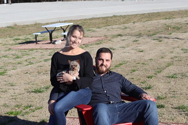 A man and woman sitting on the ground with a dog.