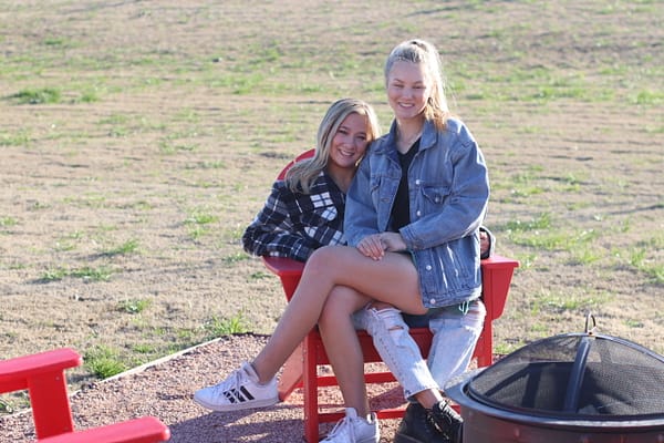 Two girls sitting on a red bench in the sun.