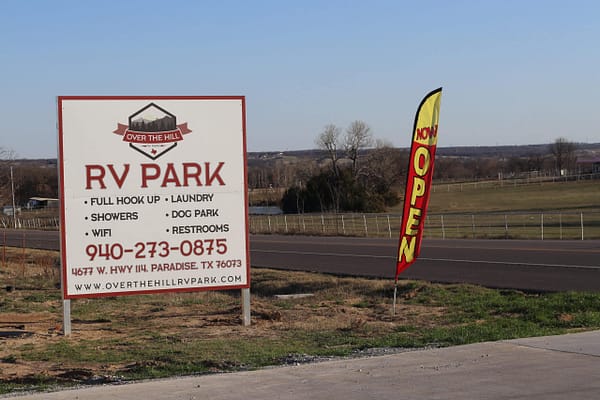 A sign for the rv park is posted next to an open flag.